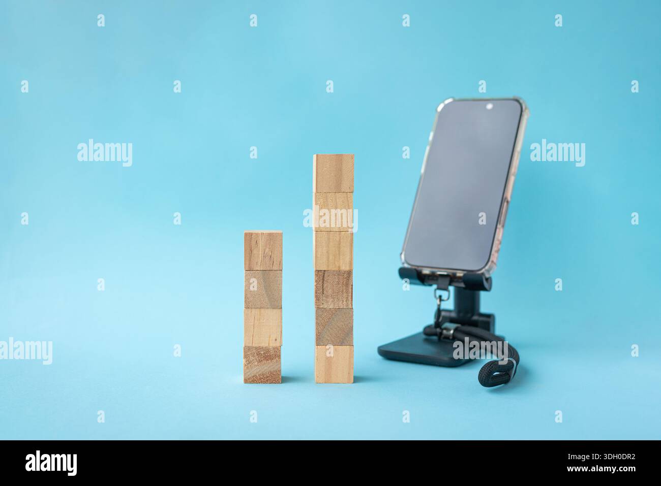 Quadratische Holzblöcke in zwei Sets neben dem Smartphone. Auf hellblauem Hintergrund. Stockfoto