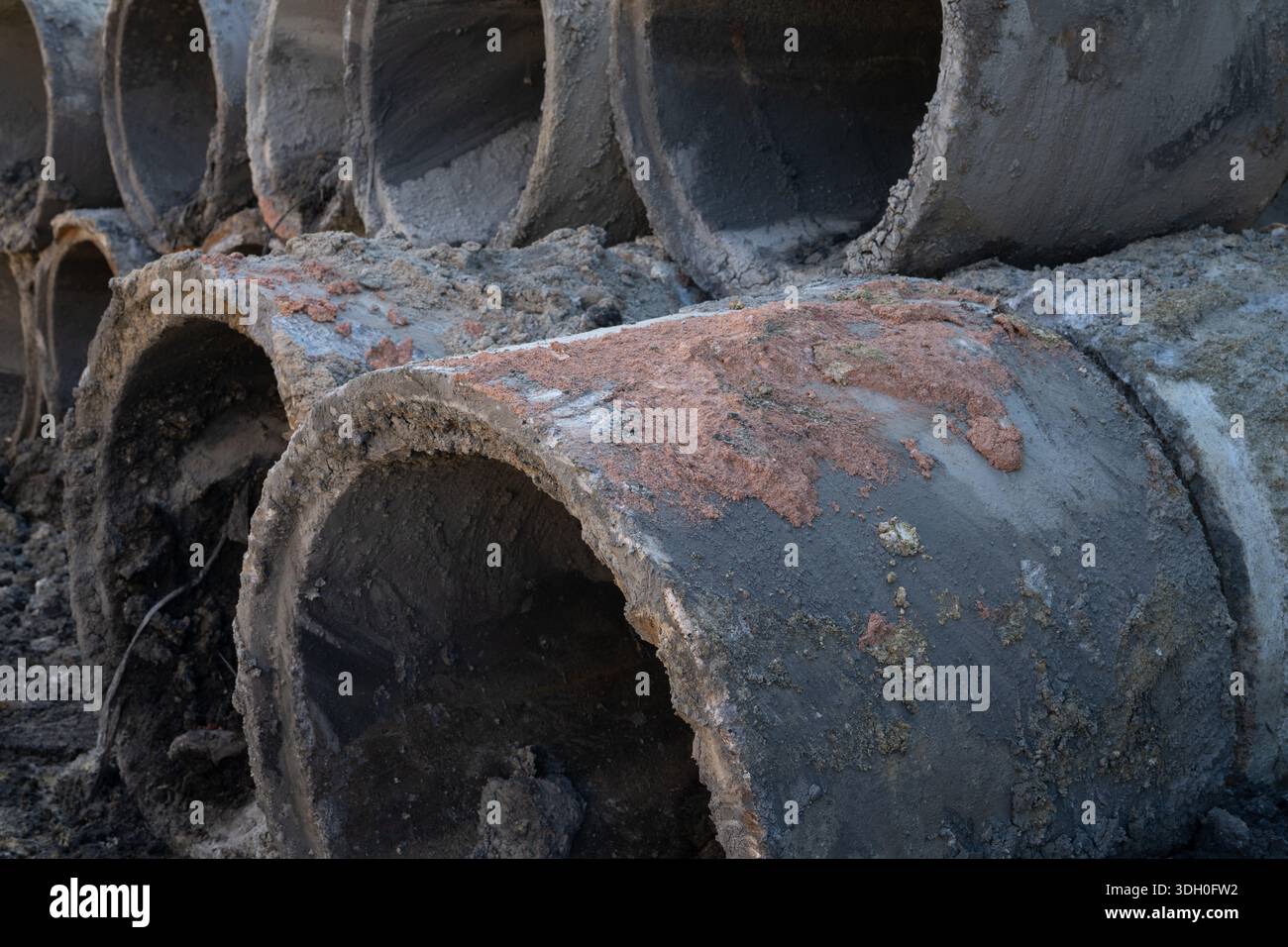 Gestapelte Betonabflussrohre auf der Außenbaustelle. Städtische Infrastrukturentwicklung, Tiefbau und Regenwassermanagement Stockfoto