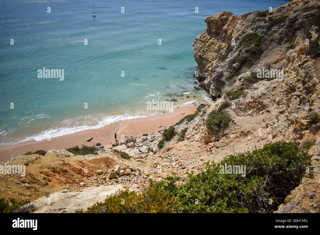 Blick von einer Küstenklippe mit Blick auf einen Sandstrand und das Meer, mit einer entfernten Person an der Küste und einem kleinen Boot auf dem Meer. Stockfoto