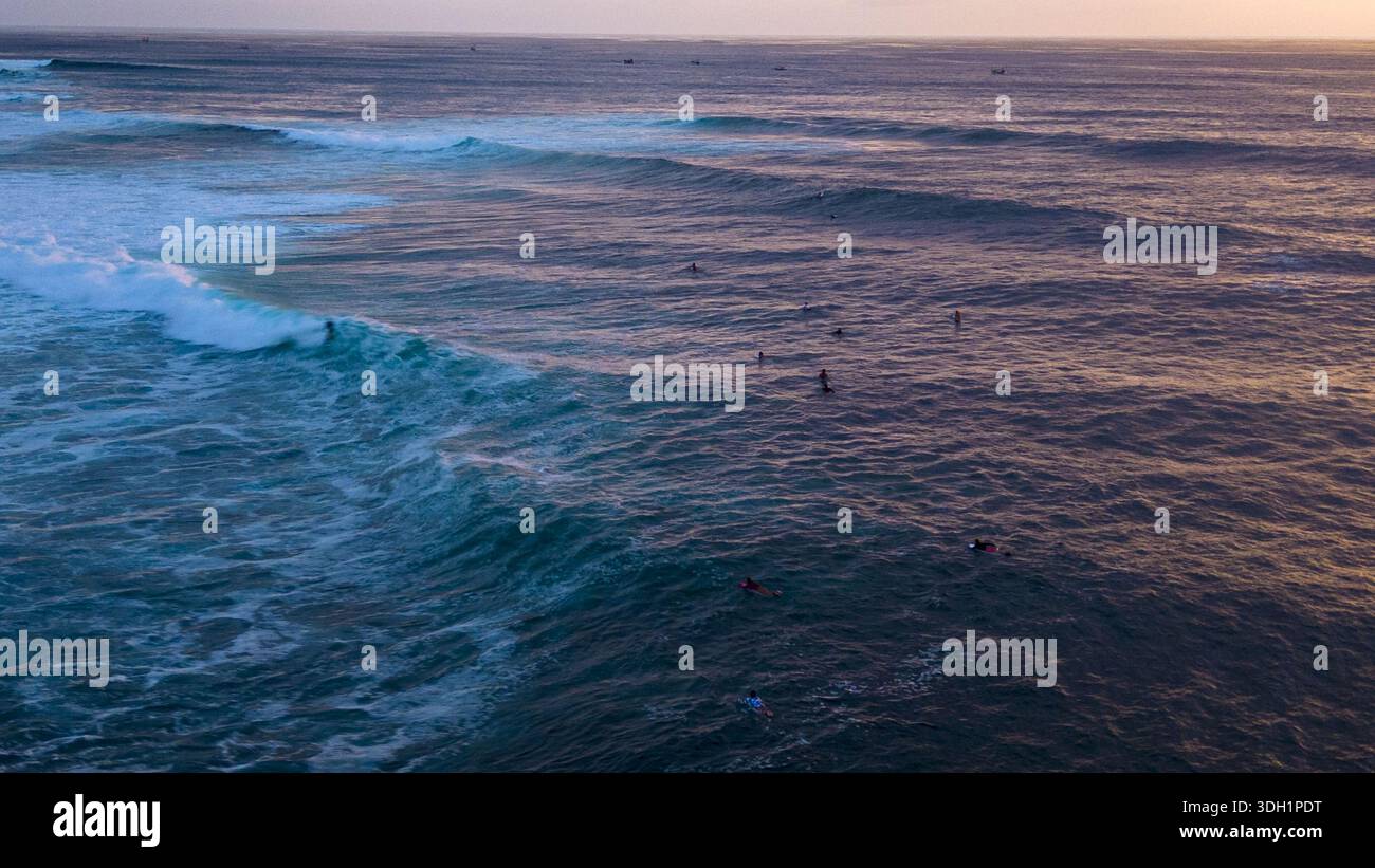 Die türkisfarbenen und indigoblauen Farben des Ozeans wirbeln mit weißem Schaum, gespickt von Surfern, die auf die perfekte Welle warten, Bali, Bali, Indonesien. Stockfoto
