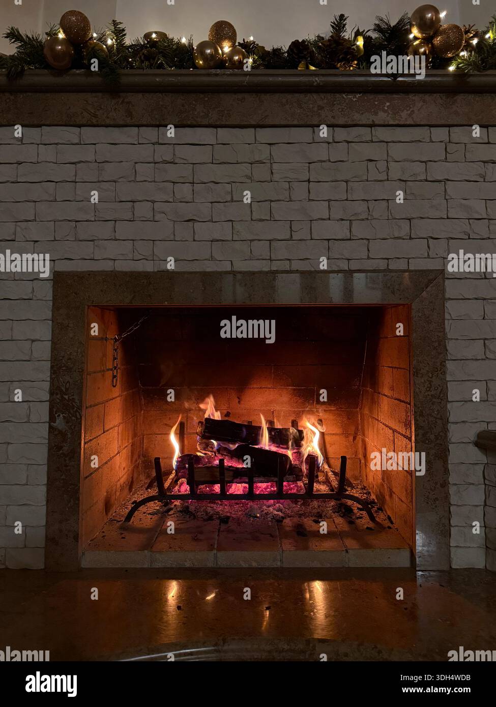 Warme Szene eines Kaminmantels mit Girlande, Lichtern und gemütlichem Kamin. Stockfoto