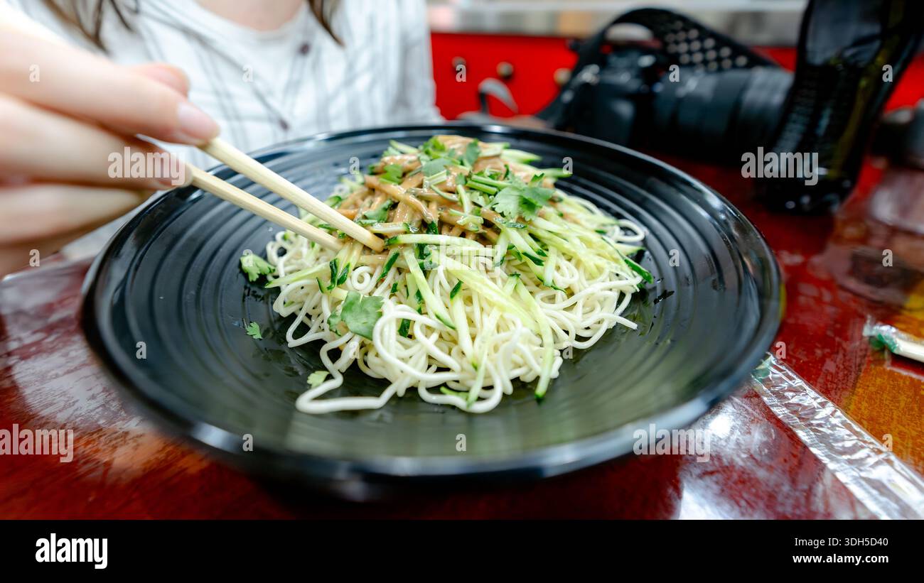 Eine Nahaufnahme eines lebhaften Gerichts mit Nudeln, garniert mit mAh Jong Sauce, serviert in einem Pekinger Restaurant. In der Präsentation werden frische Zutaten wie z. B. vorgestellt Stockfoto