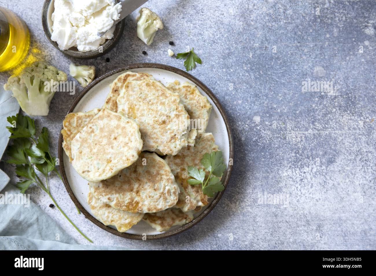 Köstliche Blumenkohlpfannkuchen serviert auf einer Keramikplatte, garniert mit frischer Petersilie. Begleitet von cremigem Ricotta und einem Spritzer Olivenöl, Perf Stockfoto