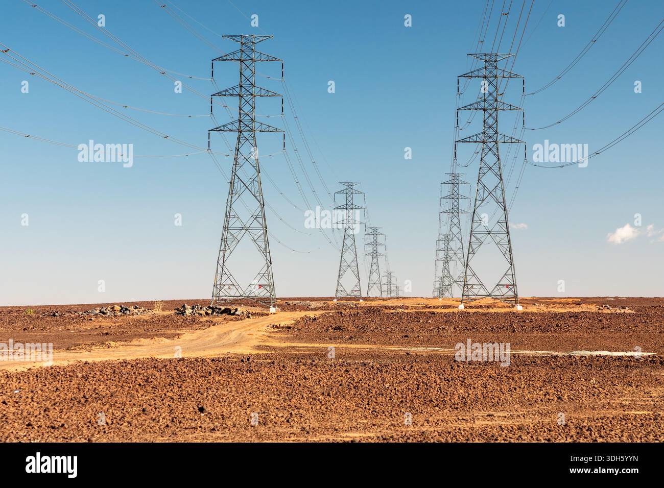 Zwei Reihen hochaufragender Strommasten durchqueren eine karge Wüste und verbinden ferne Stromnetze. Die Szene zeigt Infrastruktur, Skalierbarkeit und Stockfoto