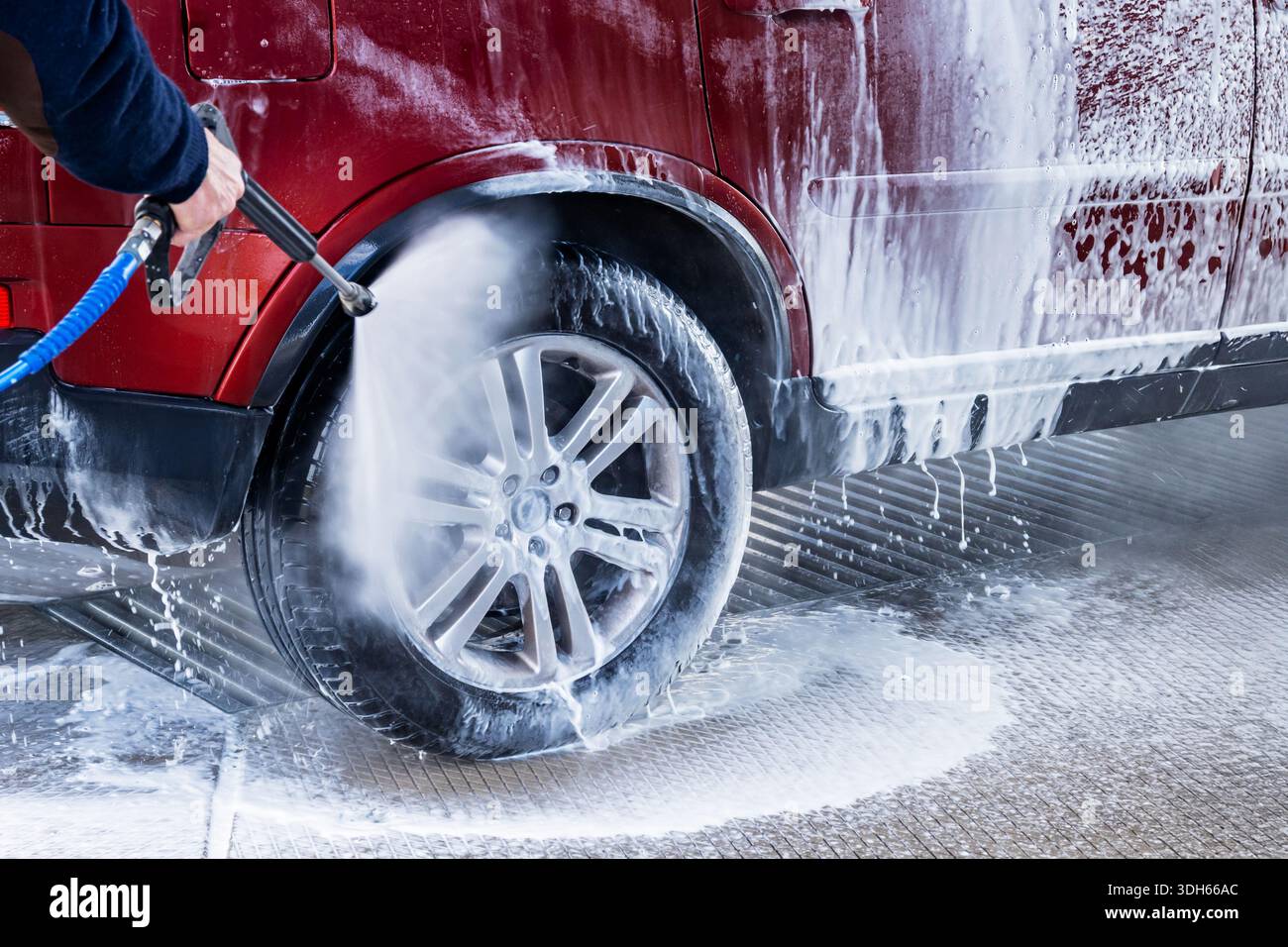 Rotes Auto in Handwaschanlage waschen. Viel Schaum auf Auto und Reifen. Stockfoto