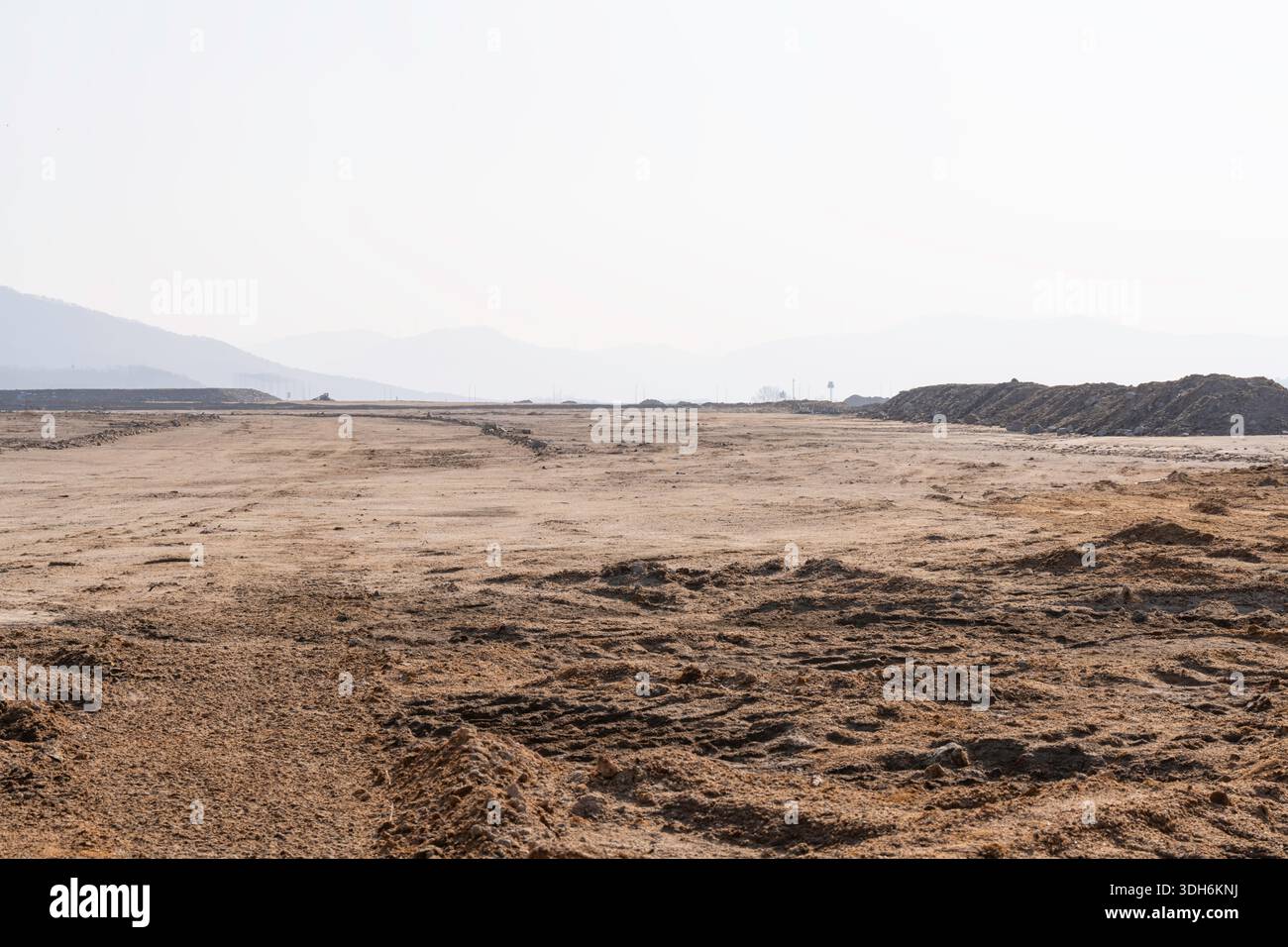 Baustelle mit unbefestigtem Weg und kargem Land unter klarem Himmel, die eine frühzeitige Infrastrukturentwicklung und weite Freiflächen für zukünftige Projekte zeigt Stockfoto