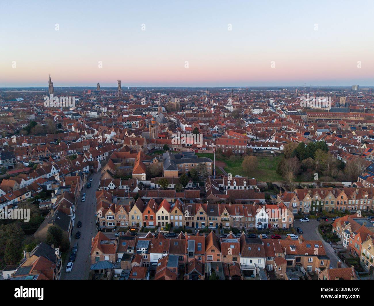 Blick aus der Vogelperspektive auf die Terrakotta-Dächer treffen auf das sanfte Licht der Dämmerung über den mittelalterlichen Türmen und bezaubernden Kanälen, Brügge, Flandern, Belgien. Stockfoto