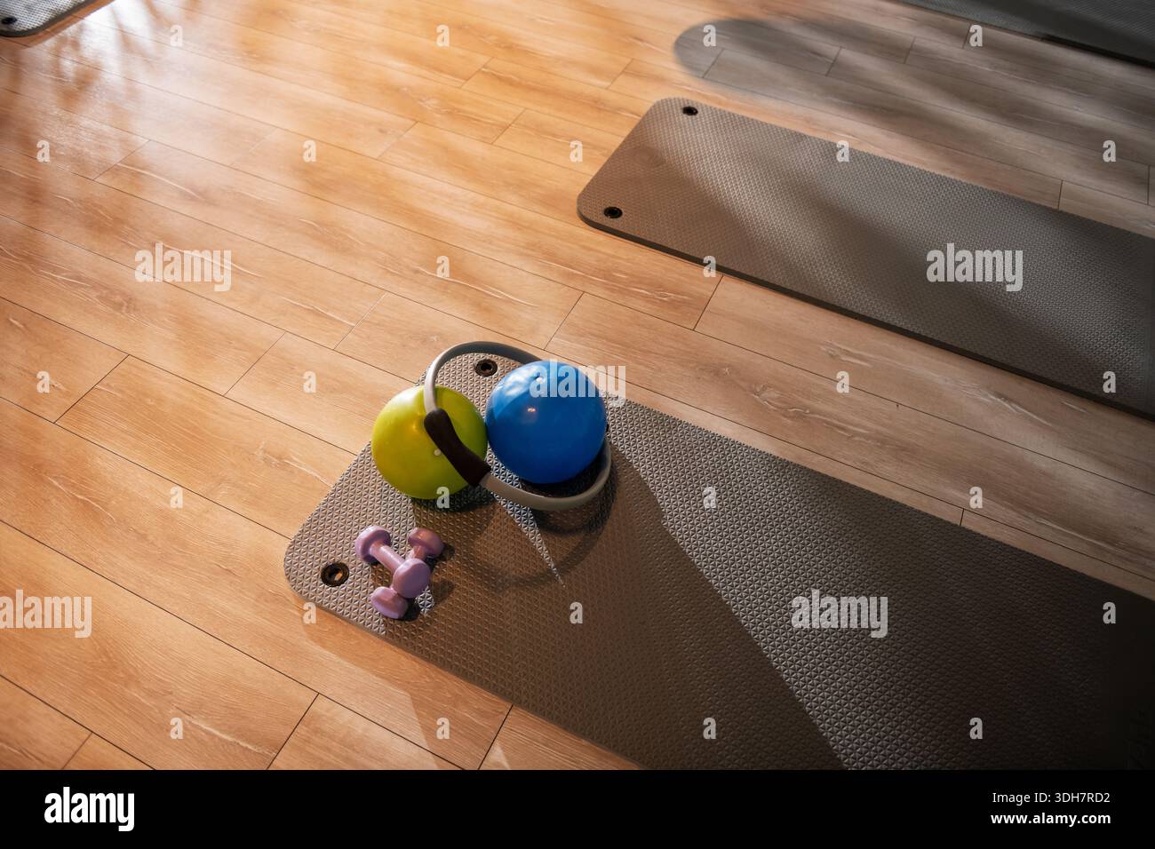 Ein Foto von einem Yoga-Studio-Boden mit Spreizmatten, einer Matte mit zwei Kurzhanteln, zwei Pilates-Bällen und einem Pilates-Ring, der ordentlich für ein Fitness s angeordnet ist Stockfoto