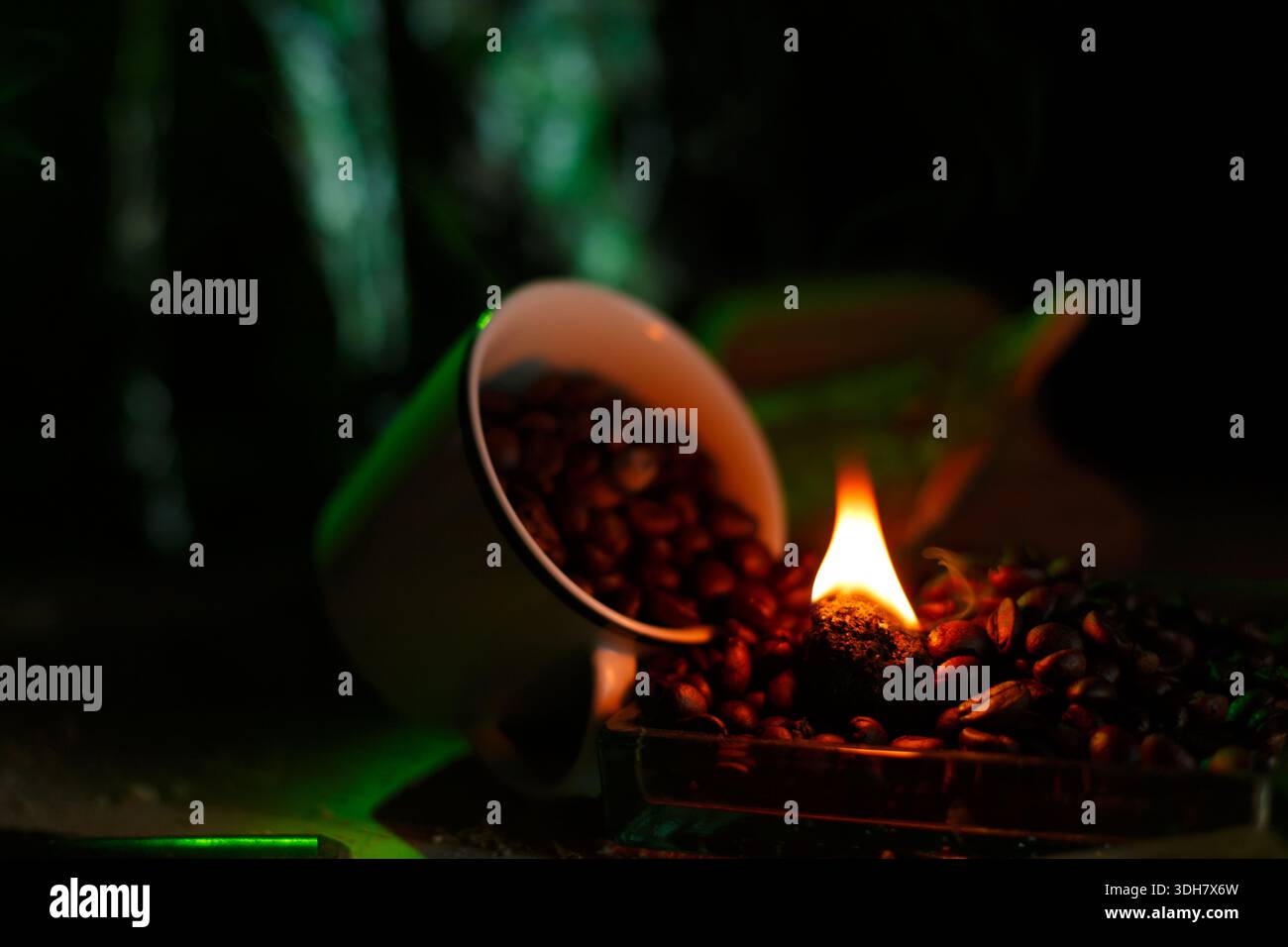 Kaffeebohnen, die aus der Tasse neben einem kleinen brennenden Emblem verschüttet werden, erzeugen eine aromatische Szene Stockfoto