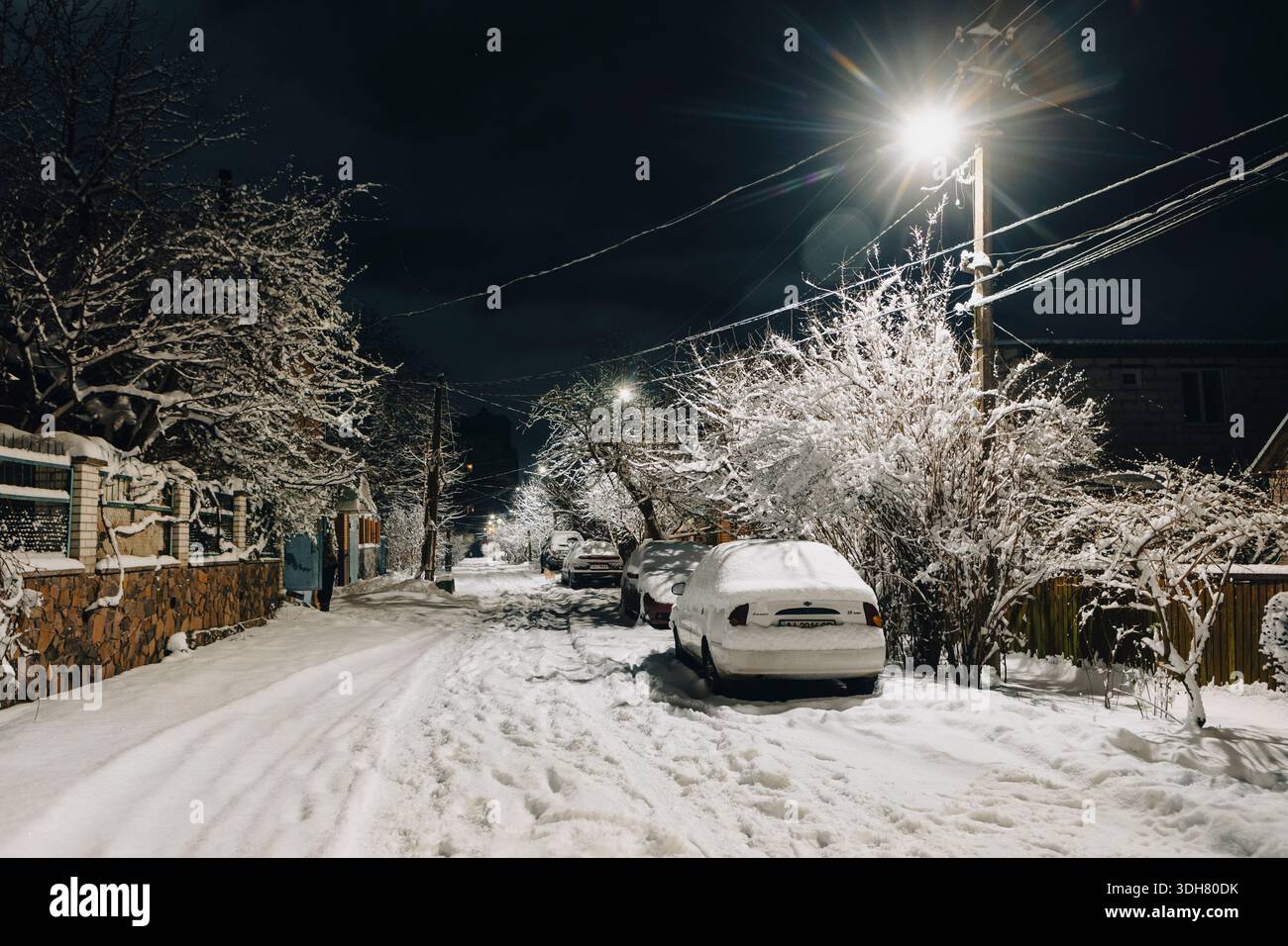 Eine winterliche Abendstraße in einer kleinen Stadt mit schneebedeckten Autos Stockfoto