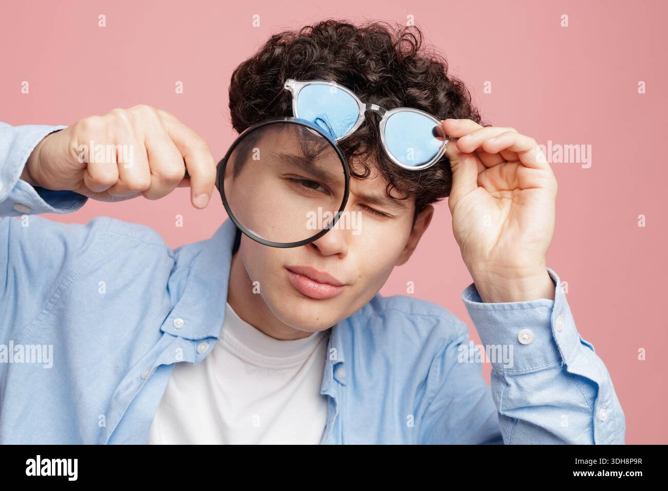 Studio-Porträt eines blinkenden jungen Mannes mit Lupe und Brille, die schlechte Sehsichtigkeit und das Konzept der Augenuntersuchung zeigen Stockfoto