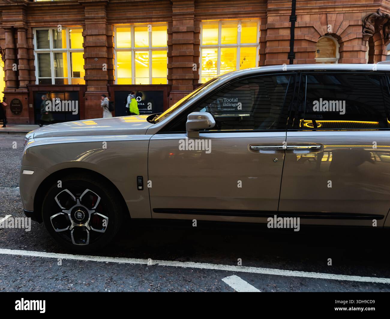 Manchester, Großbritannien - 14. Januar 2026: Ein luxuriöser Rolls-Royce Cullinan SUV befindet sich auf einer Stadtstraße neben einem Backsteingebäude mit warmgelben Fenstern und Stockfoto