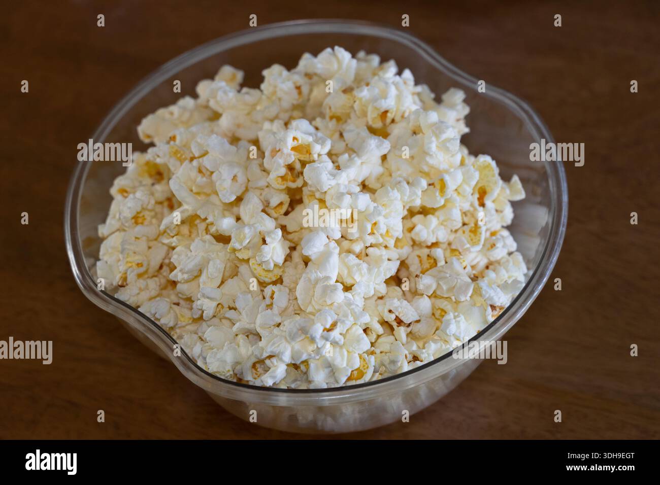 Eine Schüssel mit frisch gepresstem Mikrowellen-Popcorn in einer durchsichtigen Schüssel auf einer braunen Holzplatte. Stockfoto