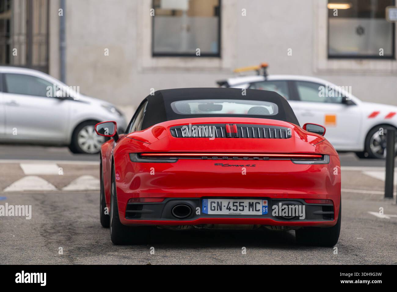Nancy, Frankreich - Blick auf einen roten Porsche 992 Carrera 4S Cabriolet, der auf einer Straße mit geparkten Autos im Hintergrund fährt. Stockfoto