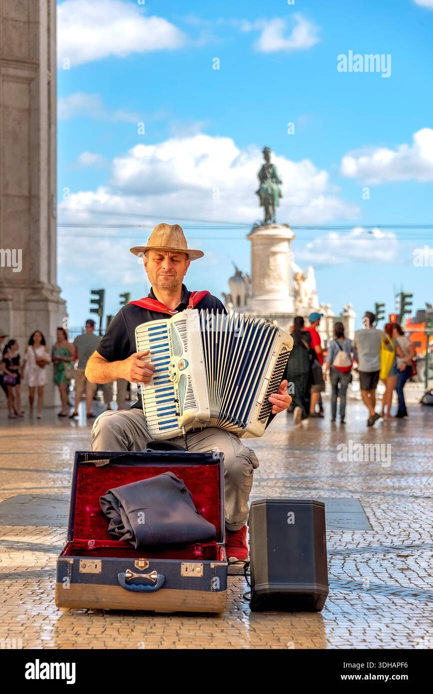 Lissabon, Portugal, 13. Juni 2023: Ein Straßenmusiker mit Strohhut spielt in der Prac do Comércio ein weißes Akkordeon mit offenem Instrumentenkoffer. Stockfoto