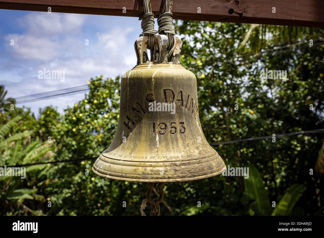 Adamstown, Pitcairn Islands - 02. Januar 2026: Blick auf die verwitterte Glocke „H.M.S. Dainty 1953“, die vor einem Hintergrund von üppigen, lebhaften G aufgehängt wird Stockfoto