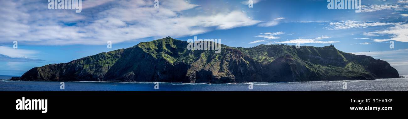 Der Blick auf eine üppig grüne Insel erhebt sich majestätisch vom glitzernden blauen Meer unter einem hellen Himmel mit Wolken, Adamstown, British Overseas Territo Stockfoto