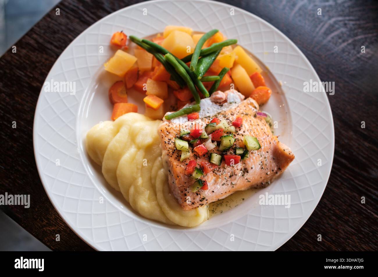 Gourmet-Teller mit gegrilltem Lachsfilet und frischer Salsa, serviert mit cremigem Kartoffelpüree und bunt gedämpftem Gemüse auf Keramikplatte Stockfoto