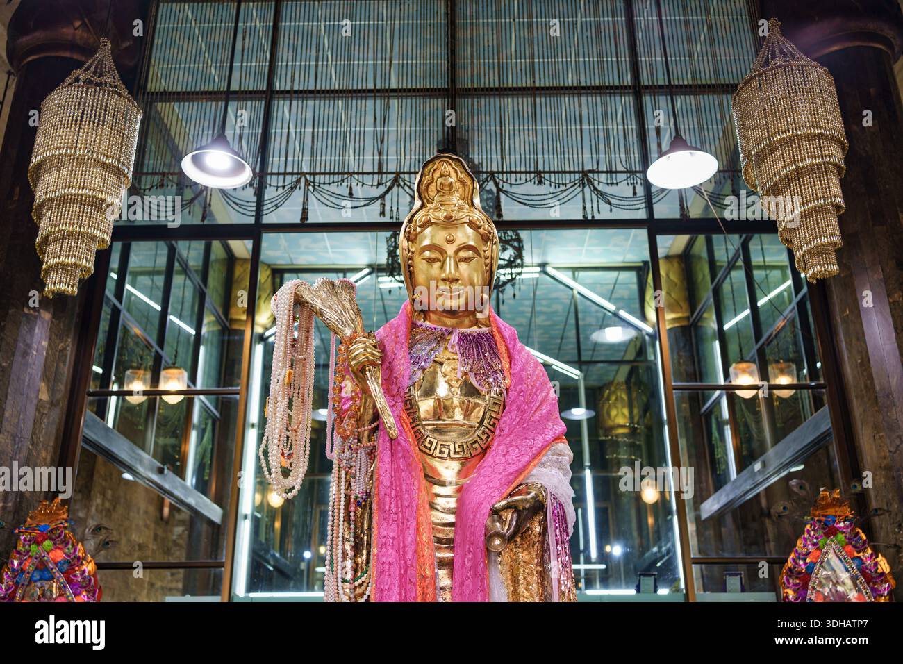 Vorderansicht der goldenen Guan Yin-Tatue mit dekorativem Stoff und Perle, Schauspiel im zeitgenössischen Glasschrein in Wat Nong Hoi, Ratchaburi, Thaila Stockfoto