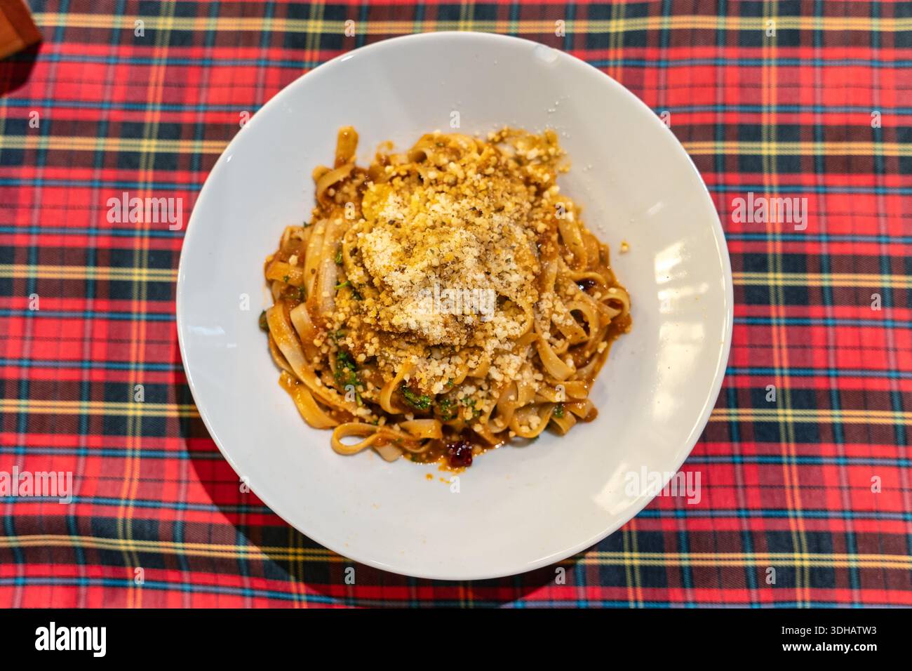 Gekochte Tagliatelle-Pasta mit herzhafter Fleischsoße und Käse auf weißem Teller auf Schottentischdecke Stockfoto