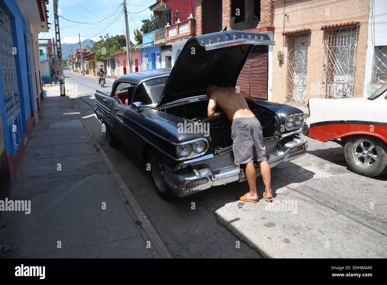 Ein Mann repariert einen Oldtimer in einer Wohnstraße in Trinidad, Kuba Stockfoto