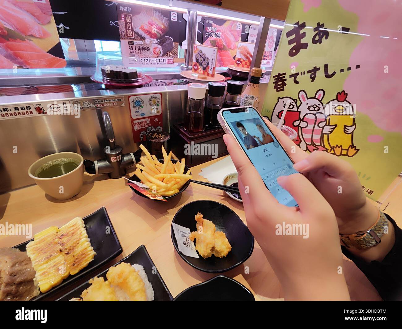 Person, die ein Foto von Tempura und Pommes in einem japanischen Sushi-Restaurant mit Förderband macht Stockfoto