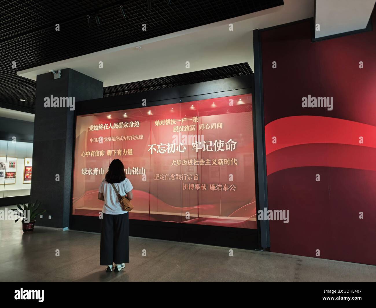 Frau, die eine Ausstellung mit rotem Thema und chinesischem Text in einem Museum oder Kulturzentrum ansieht Stockfoto
