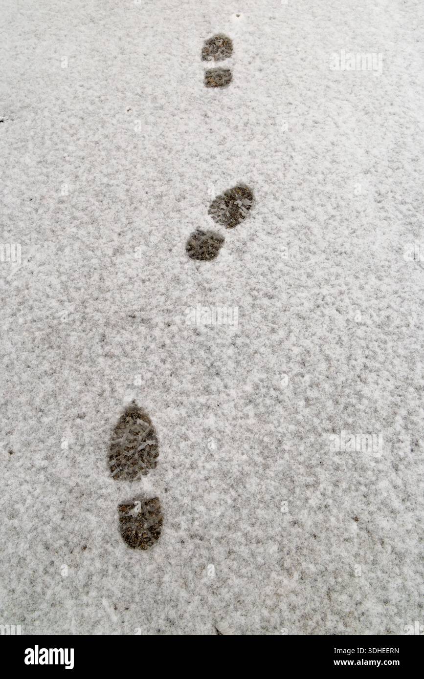 Fußabdrücke auf einer schneebedeckten Straßenoberfläche, die bei kaltem Wetter menschliche Spuren auf einer Winterstraße zeigen. Stockfoto
