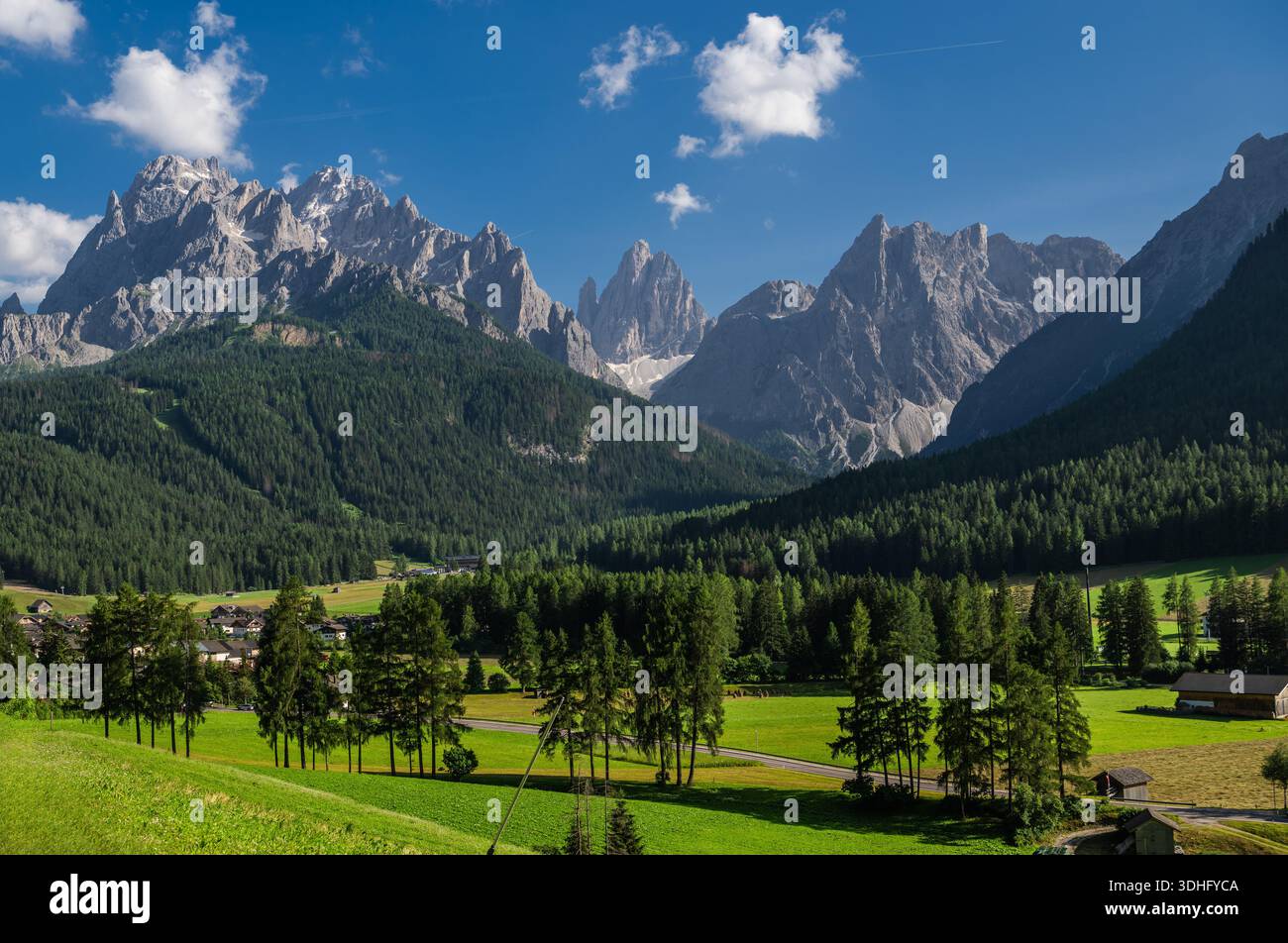 Grüne Felder erstrecken sich unter einem klaren blauen Himmel in der Nähe hoher Berge mit Bäumen. Sexten, Italien. Stockfoto