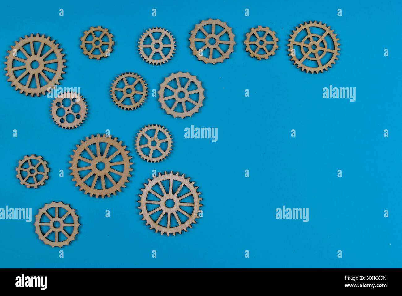Acht hölzerne Zahnräder auf blauer Oberfläche veranschaulichen mechanische Verbindungen, Bewegungsübertragung und Konstruktionsvariationen in technischen Systemen. Stockfoto