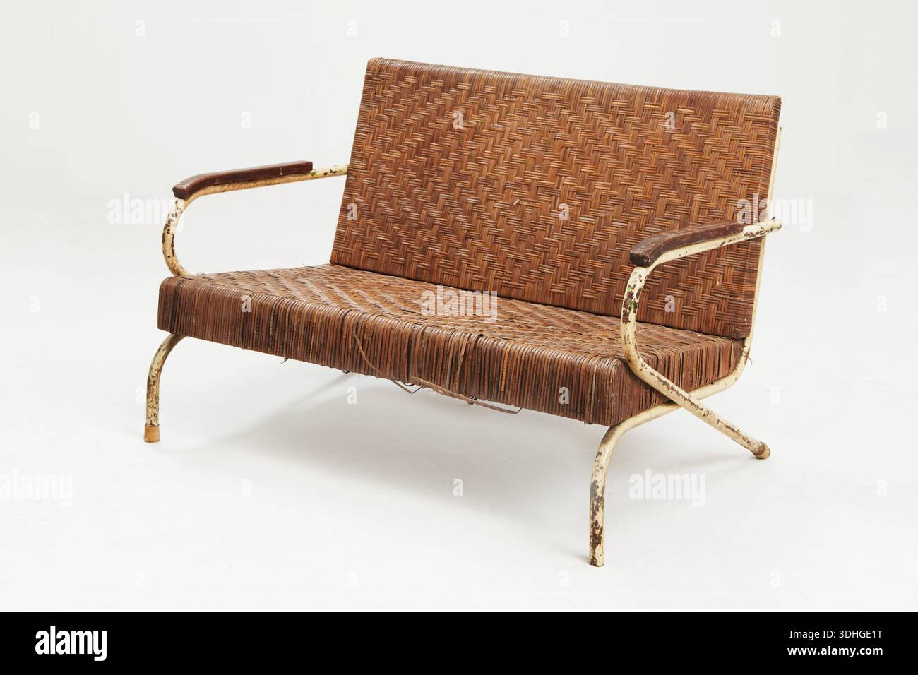 Eine Vintage-Bank aus gewebtem Rattan mit einem Metallrahmen und geschwungenen Armlehnen, die Zeichen von Alter und Patina zeigt, isoliert auf einem hellgrauen Hintergrund Stockfoto