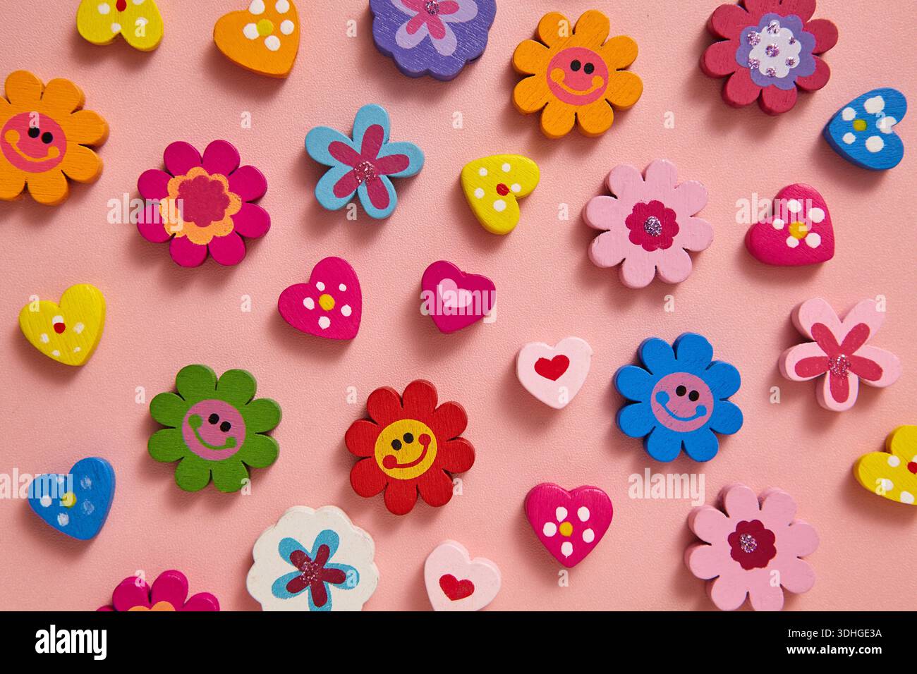 Eine lebendige flache Lage aus farbenfrohen Perlen, Blumen und Herzen mit fröhlichen Mustern und Smiley-Gesichtern auf weichem rosa Hintergrund. Valentinstag Stockfoto