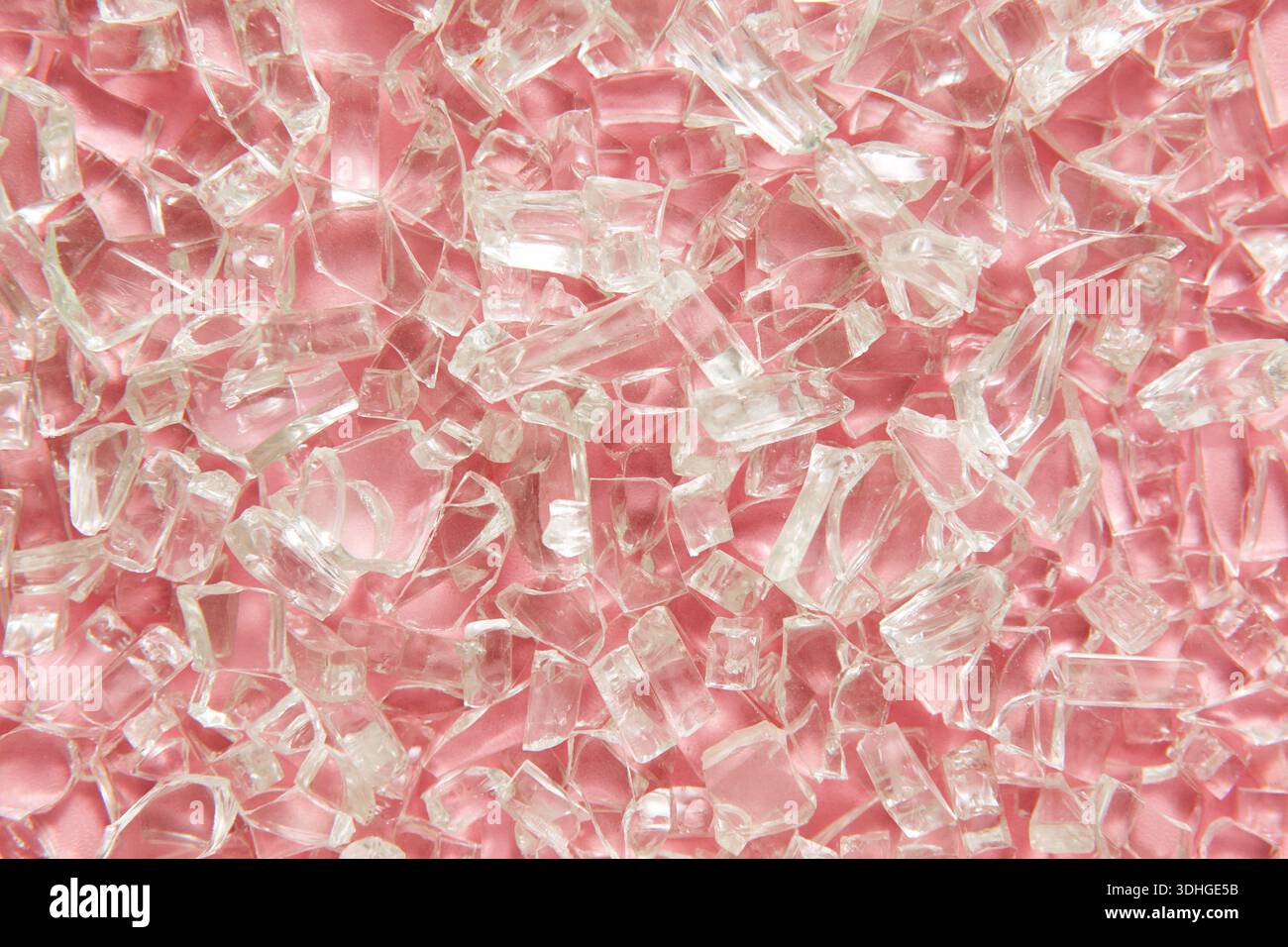 Eine Makroansicht von klaren, gebrochenen Glasstücken auf einem sanften rosa Hintergrund, die eine strahlende abstrakte Textur erzeugen Stockfoto