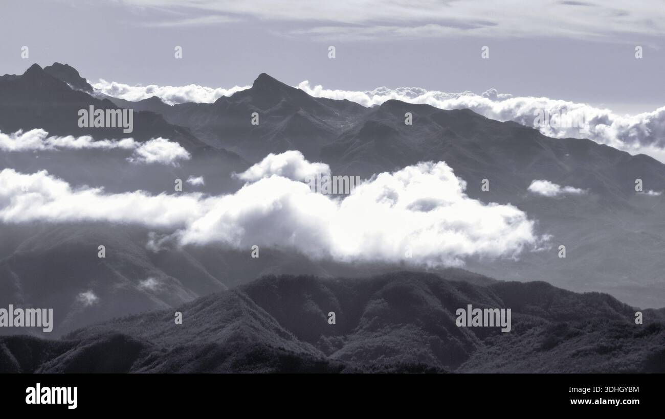 Eine dramatische, entsättigte Landschaft des italienischen Apennins in großer Höhe, wo zerklüftete Gipfel durch eine dichte Schicht weißer Wolken durchdringen. Stockfoto