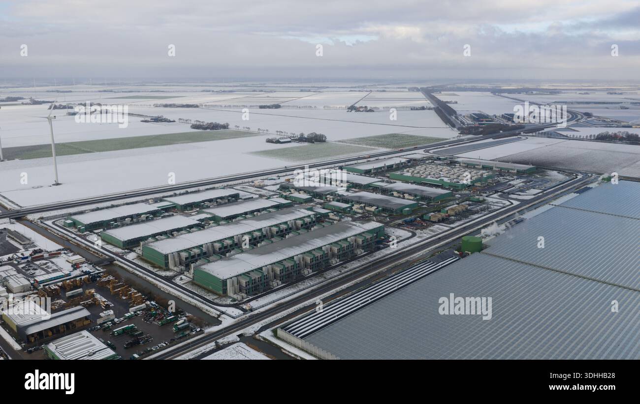 Aus der Vogelperspektive eines weitläufigen Rechenzentrumskomplexes, eingebettet in schneebedeckte Felder unter grauem Himmel, ein krasser Kontrast von Industrie und Natur, Middenmeer, Stockfoto