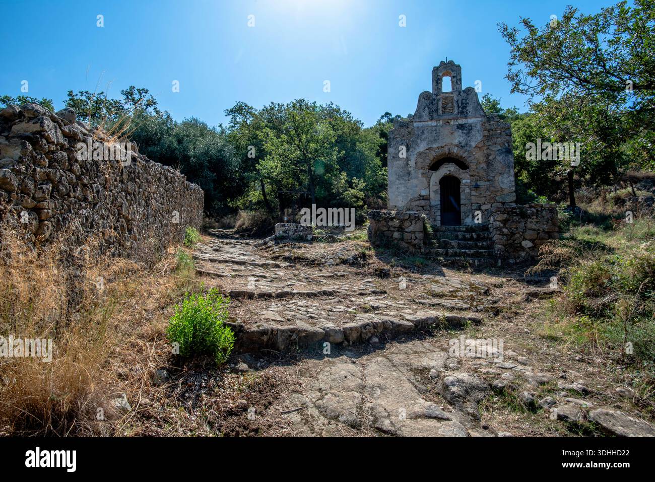 Steinkapelle mit eisernem Kreuz entlang eines ländlichen Weges in der Nähe von Corte, Korsika, Frankreich. Historische religiöse Architektur in mediterranen Wäldern, ideal für Stockfoto