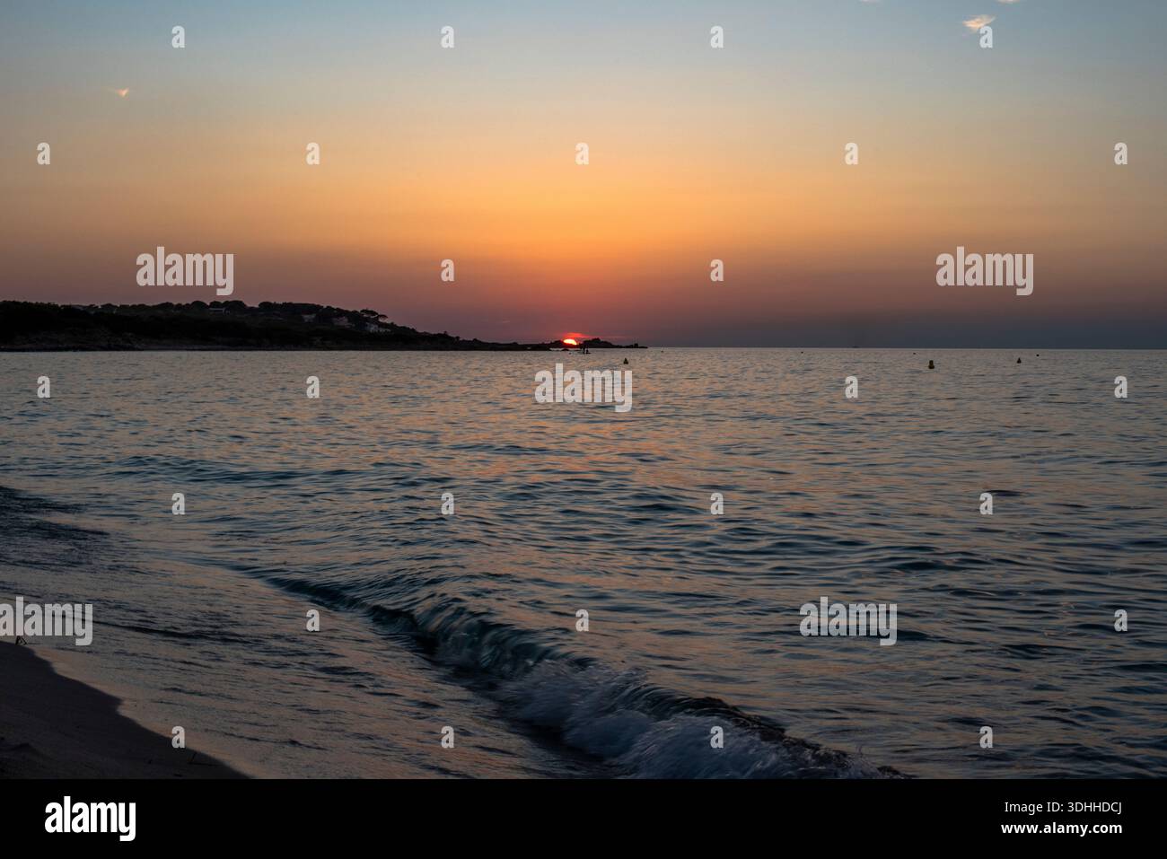 Goldener Sonnenuntergang am Horizont über einem ruhigen Mittelmeer in Korsika, Frankreich. Sanfte Wellen und warme Töne sorgen für eine friedliche Küstenlandschaft Stockfoto