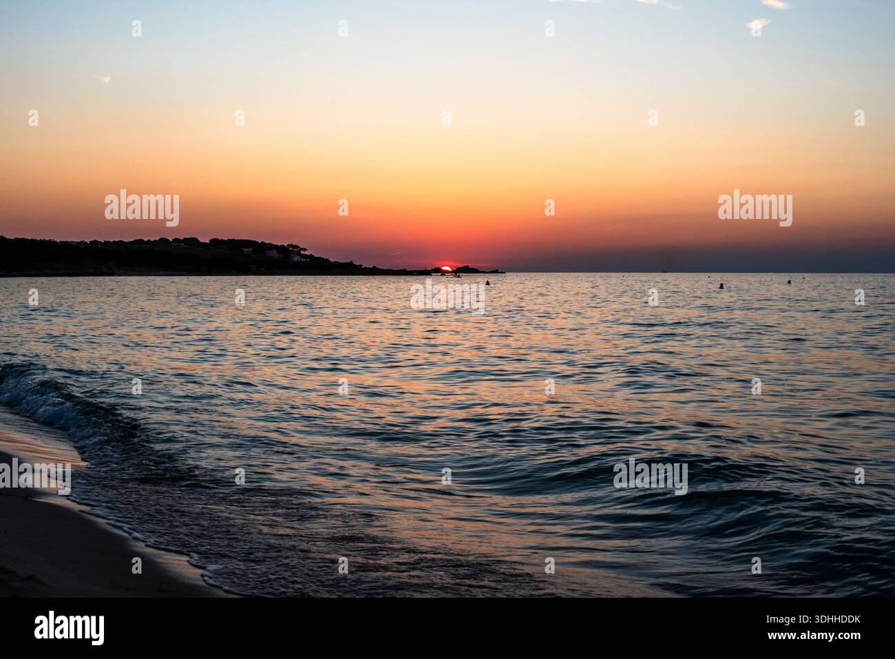 Niedrige Sonne berührt den mediterranen Horizont bei Sonnenuntergang in Korsika, Frankreich. Sanfte Gefälle und ruhiges Wasser sorgen für eine ruhige Küstenlandschaft, ideal für Wellness Stockfoto