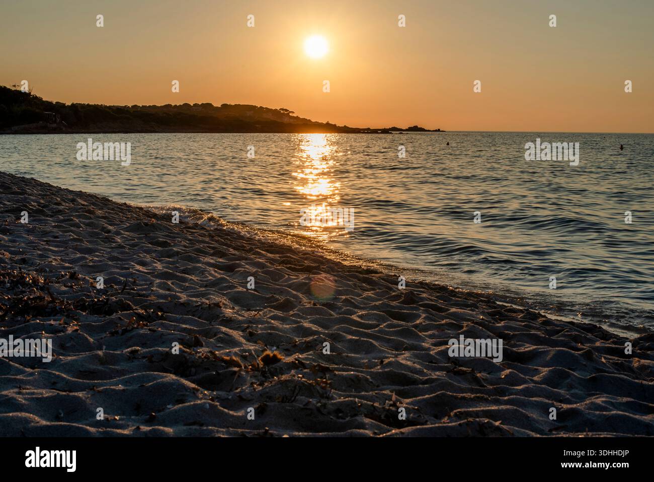 Warmes Licht bei Sonnenuntergang reflektiert auf sanften Wellen entlang eines mediterranen Sandstrandes in Korsika, Frankreich. Eine ruhige Küstenlandschaft, ideal für Reisen, Wellness und Stockfoto