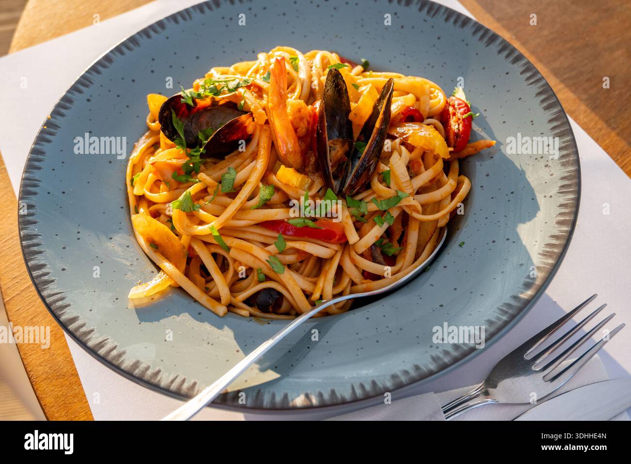 Linguine mit Meeresfrüchten und Gemüse (Muscheln, Garnelen, Tomaten, Knoblauch) auf Teller mit Löffel und Gabel. Stockfoto