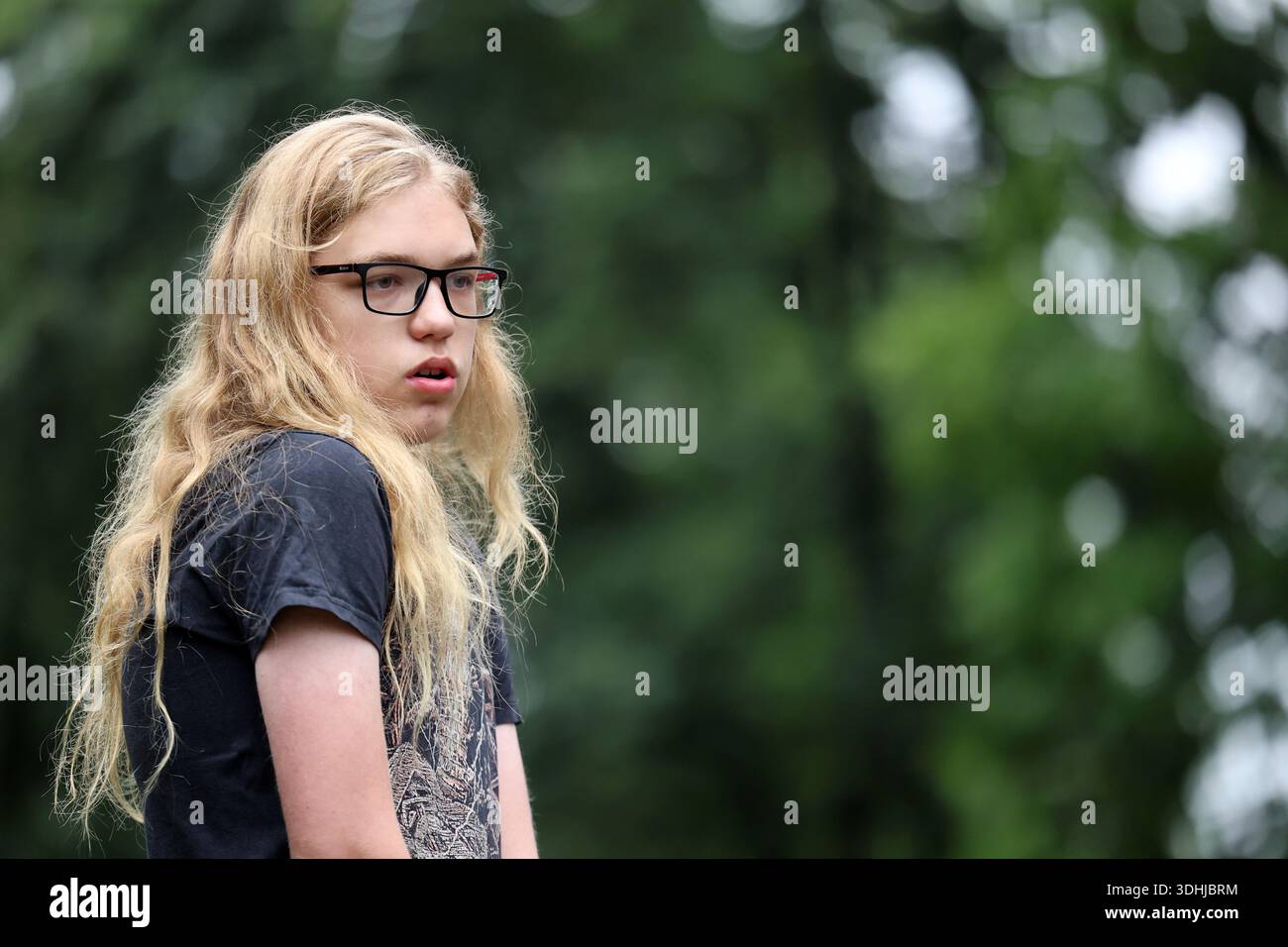 Nachdenkliche blonde Jugend mit einer Brille, die draußen seitlich schaut Stockfoto