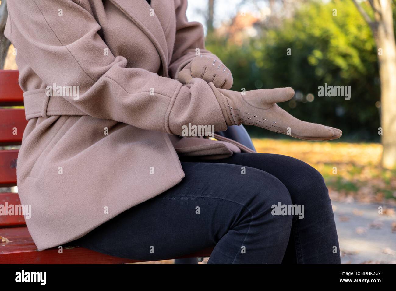 Nahaufnahme der Hände einer Frau, die einen hellbraunen, mit Nieten versehenen Handschuh anpassen, auf einer Holzbank sitzen und die Vorbereitung auf kaltes Wetter und schicke Sturzzugänge reflektieren Stockfoto