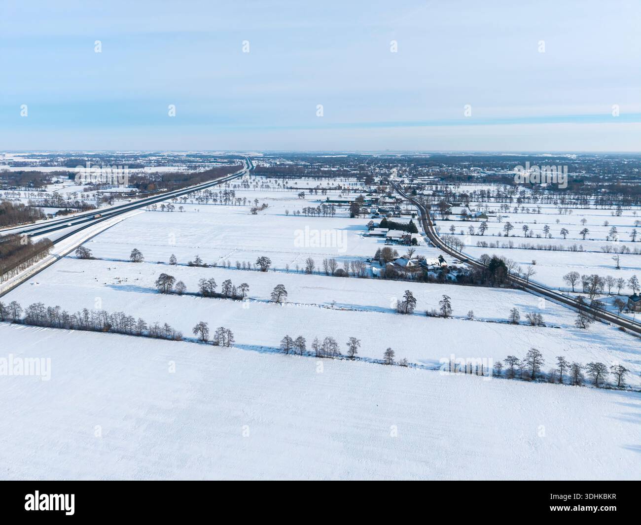Ausgedehntes, verschneite Gelände mit geometrischen Feldabteilungen und verstreuten dunklen Bäumen. Stockfoto