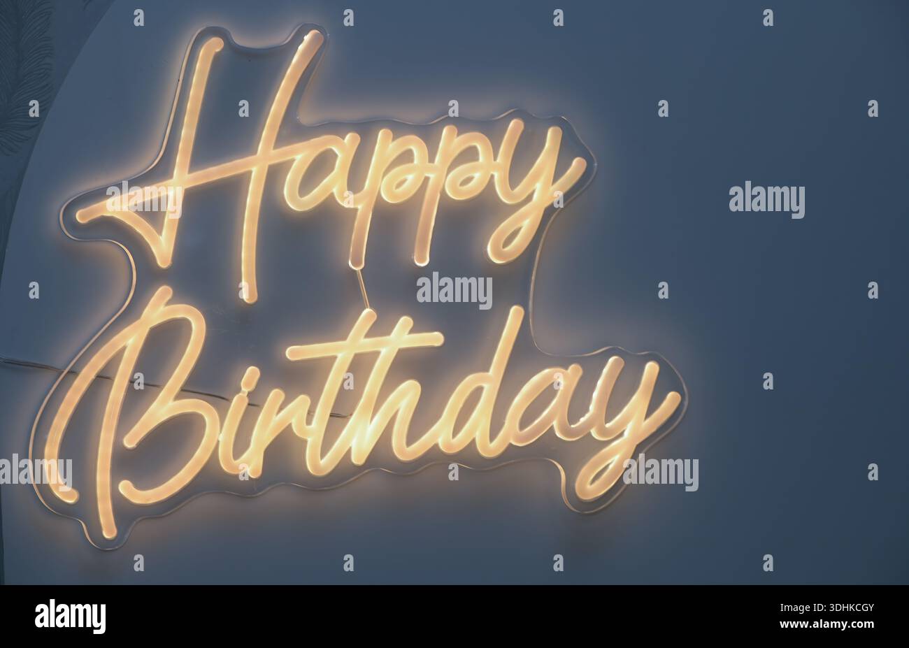 Ein Neonschild mit der Aufschrift Happy Birthday. Das Schild leuchtet auf und leuchtet gelb. Das Schild ist auf blauem Hintergrund Stockfoto