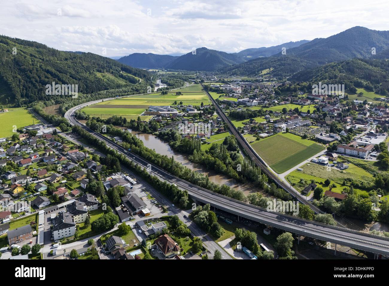 Aus der Vogelperspektive auf die Mur, die sich durch das Tal schlängelt, im Kontrast zu den geraden Linien der Autobahn und den üppigen grünen Bergen Peggau-Deuts Stockfoto