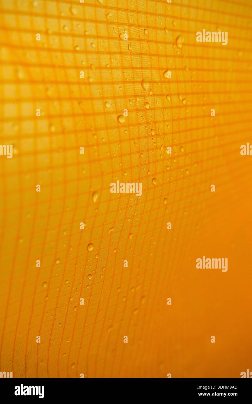 Regentröpfchen auf wasserdichtem Zeltgewebe erzeugen eine detaillierte Textur für den Außenbereich mit Gittermuster und warmen Tönen, geeignet für den Hintergrund Stockfoto