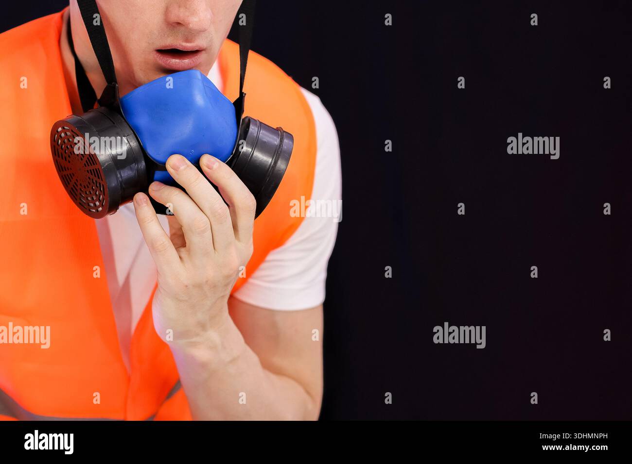 Fokussiertes Bild einer Person in Sicherheitsausrüstung, die bei schwachem Licht das Ausatemventil der blauen Atemschutzmaske einklemmt und sich auf dem Gesicht einstellt Stockfoto