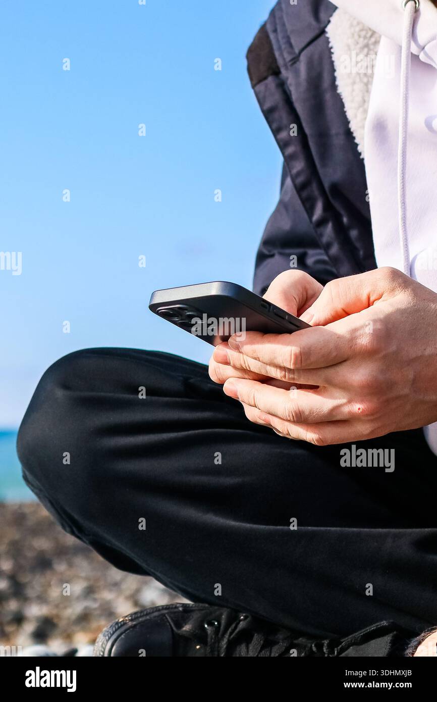 Hände greifen tragbares Gerät vor dem Meereshorizont und symbolisieren Technik in natürlicher Umgebung. Stockfoto