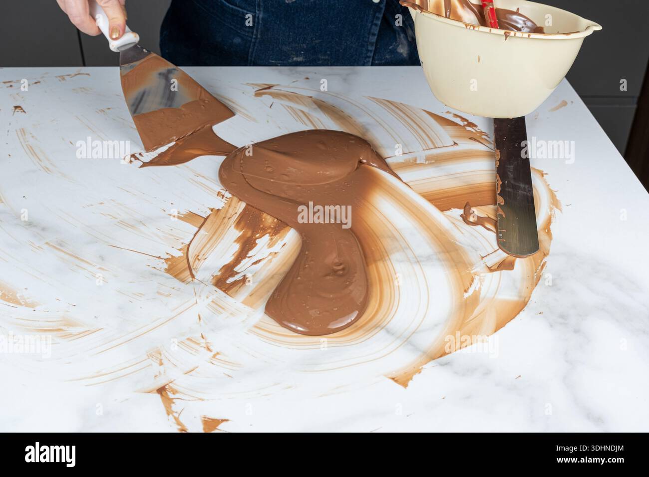 Eine Konditorin, die Schokolade auf einer Marmorarbeitsfläche temperiert. Stockfoto