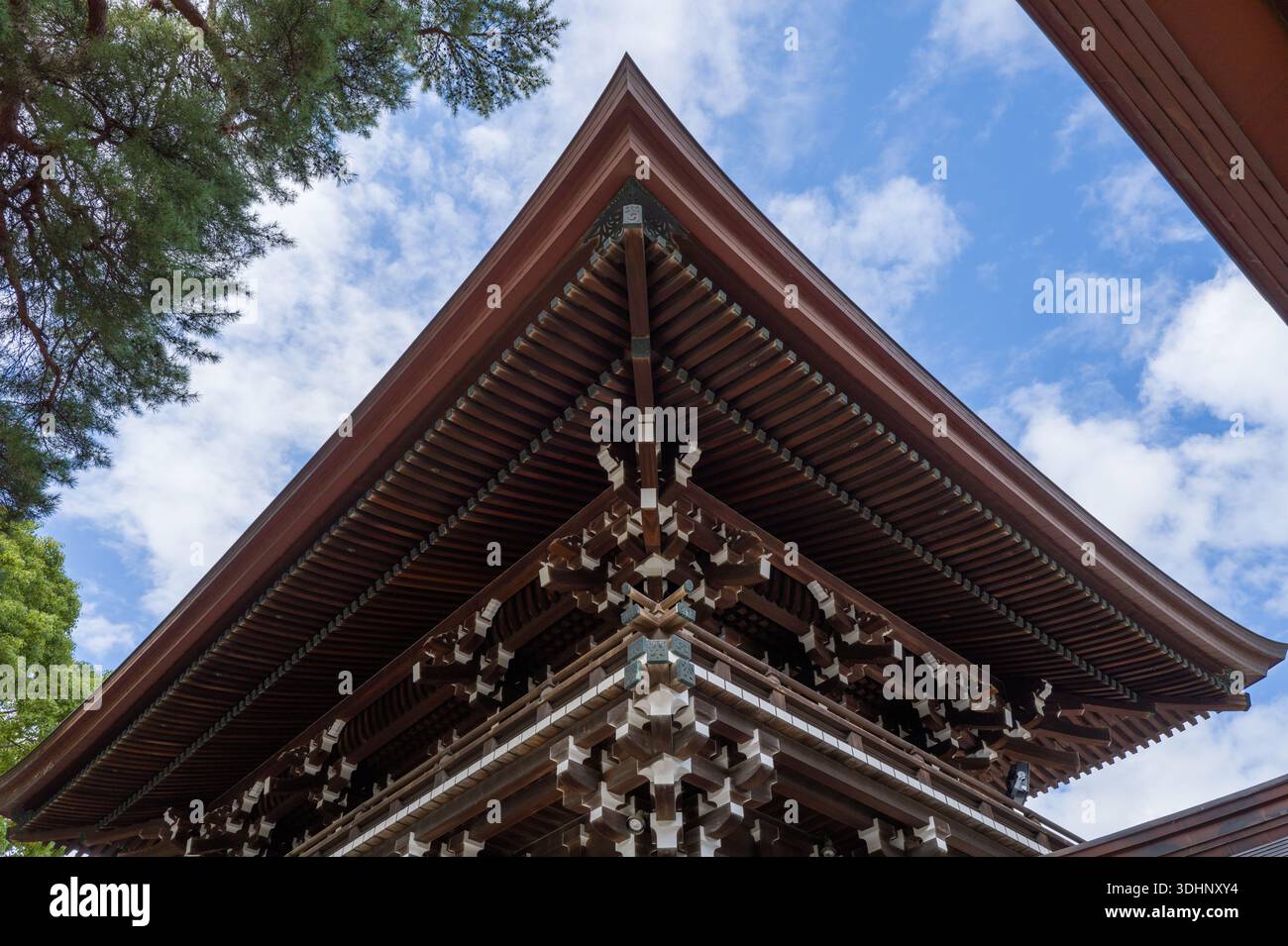 Tokio, Japan - 21. Oktober 2024: Das Bild zeigt eine Nahaufnahme der komplizierten hölzernen Dachkonstruktion eines Gebäudes am Meiji Jingu-Schrein mit blauem Himmel und Wolken im Hintergrund. Stockfoto